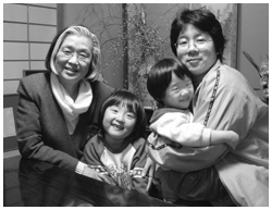 写真:仏壇の前で長男・真木さんの妻 啓子さん、孫の薫美ちゃん、陽美ちゃんと