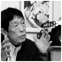 写真:山を描いた自作のスケッチ画の前で語る